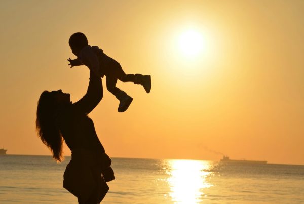 Silhouette of a mother lifting her child at a sunset beach, capturing warmth and love.